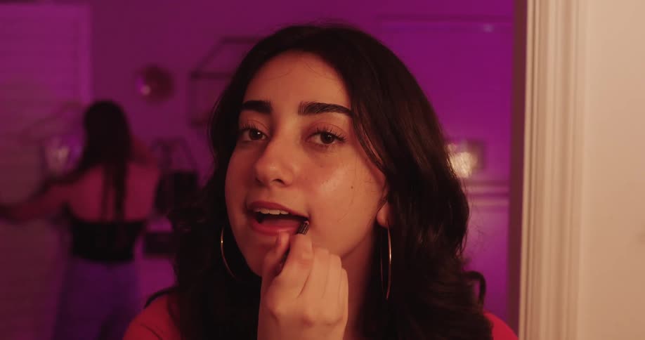 The face of a young woman looking at herself in the mirror while applying makeup to her lips