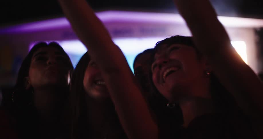 A group of teenage girls is taking a selfie and having fun at a concert at night