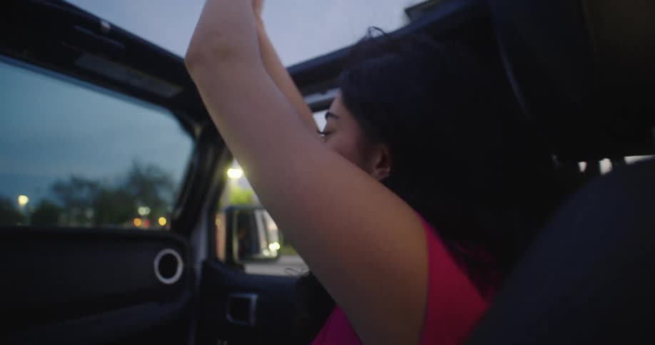 Teenage girls dancing on a moving convertible car while driving in the city at dusk