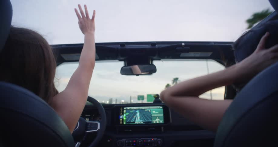 Two women in the front seat of a convertible car enjoying the vibe