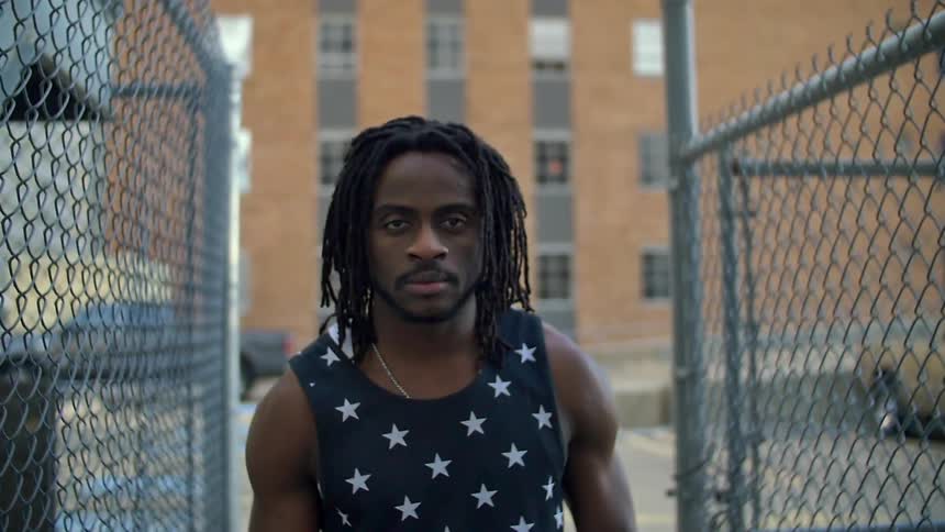 A man is standing in an alley between two fences with a building ahead