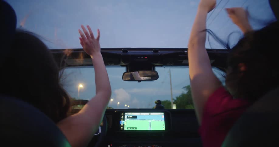 Two women with their arms up while sitting in the front seat of a moving vehicle