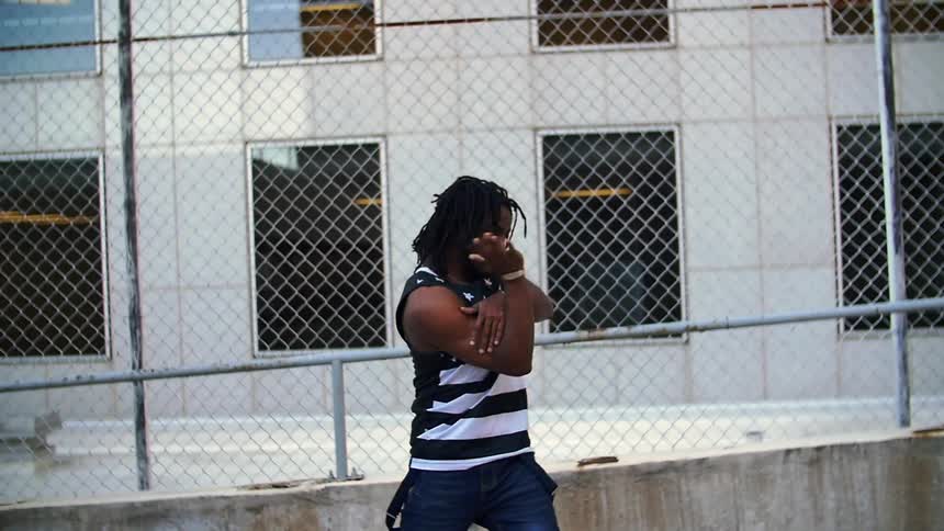 A man dances outside in front of a chain link fence