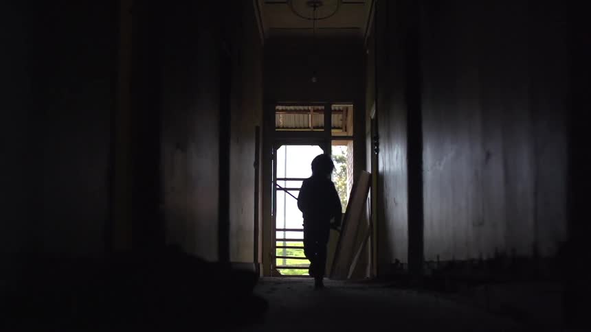 Child running down a dark hallway with a stick