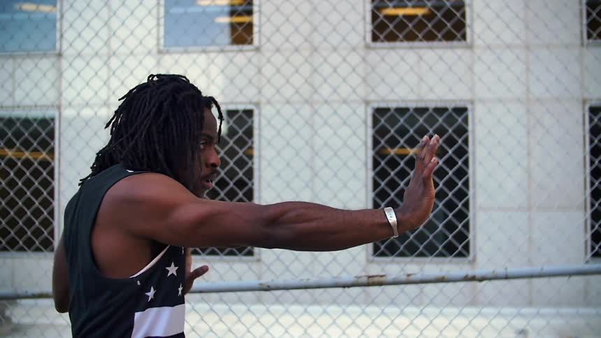 A black man is standing in front of a fence doing a dance