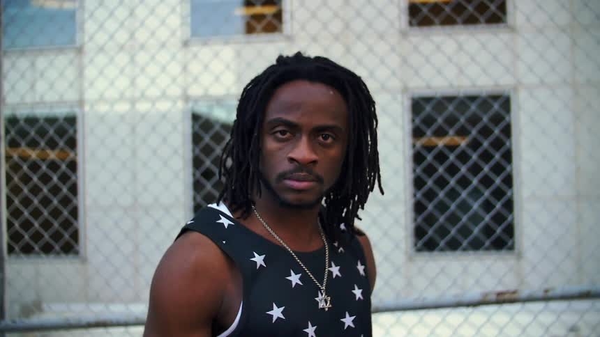 A black man is staring at the camera as he stands outside