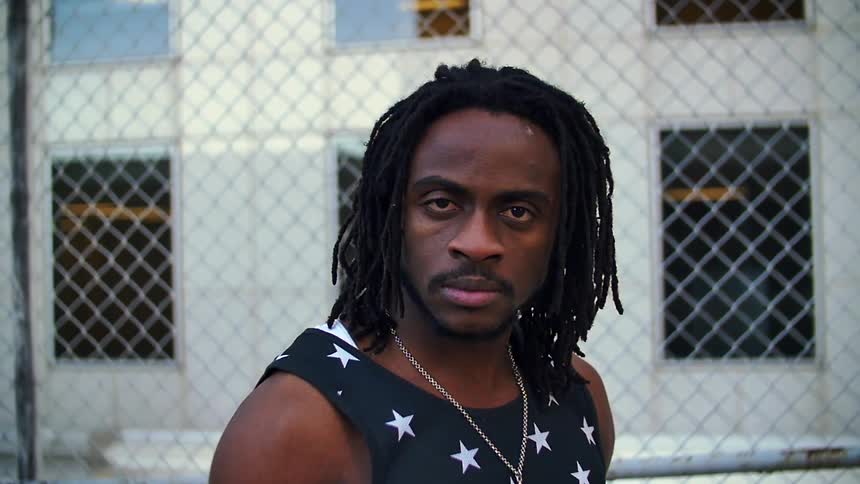 A man standing and staring in front of a chain link fence and building