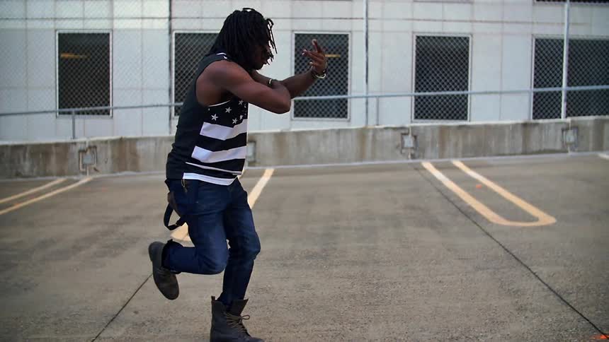 A man in a flag shirt dances in a parking lot