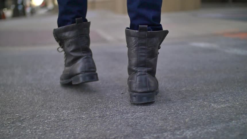 A person walking on the ground and showing a close up view of the boots