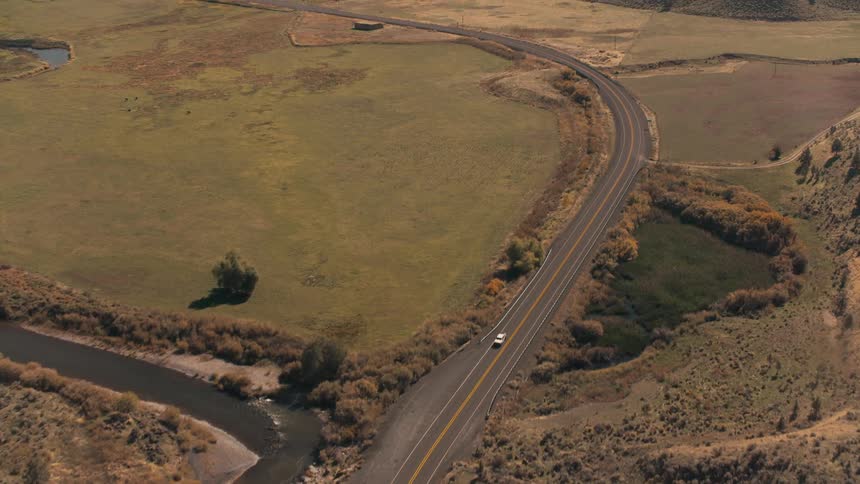 Aerial shot of some vehicles traveling along a paved road surrounded by mountains