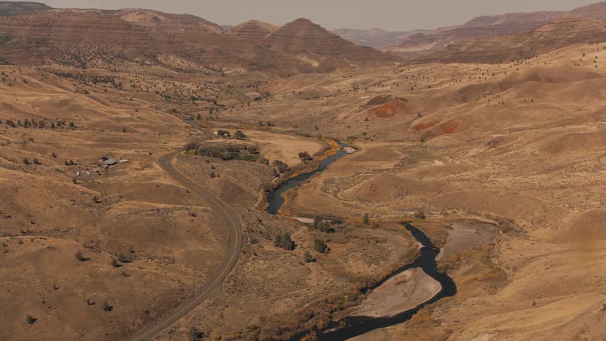 A winding river cuts through a dry hilly landscape next to a winding road as captured from an aerial perspective
