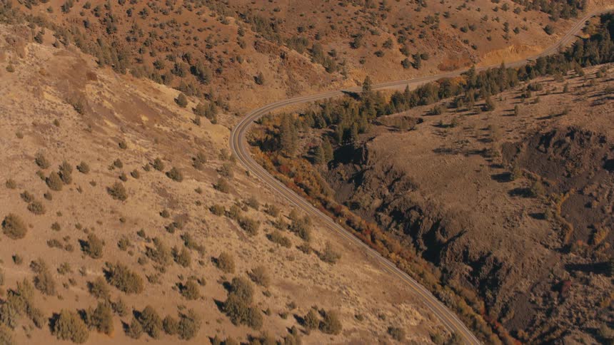 Aerial of a few cars travelling along a remote mountain highway on an autumn day