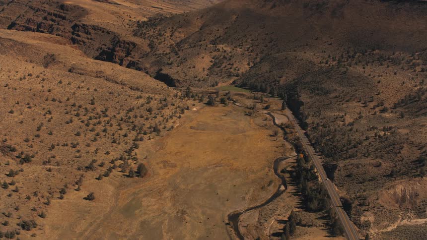 An aerial view of a desert region with an asphalt highway and some hills with some trees