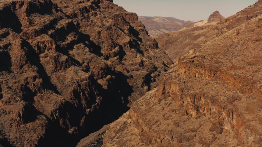 A rugged arid landscape with steep rocky hills and a deep shadowed canyon running through the center
