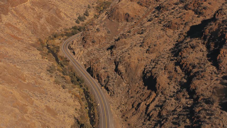 A winding road snakes through a rugged sunlit canyon