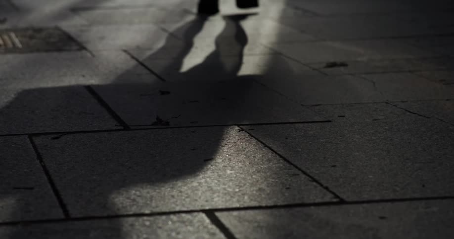 Feet of a person wearing black leather shoes walking on a concrete street
