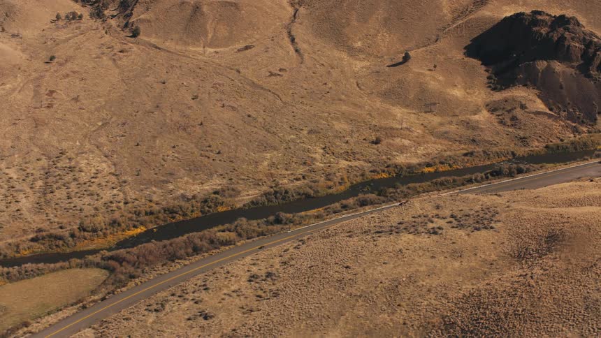 Aerial view of a winding road through a dry landscape with sparse vegetation and a river alongside
