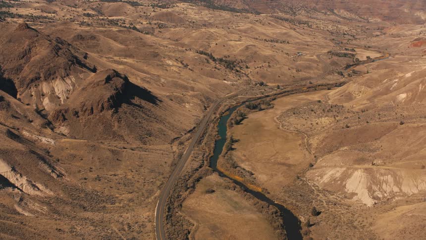 Aerial view of an arid landscape with dry mountains a river winding along the terrain and a winding road