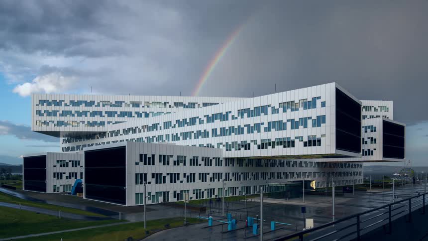 The modern angular architecture of equinor fornebu in norway stands under a cloudy sky featuring a rainbow