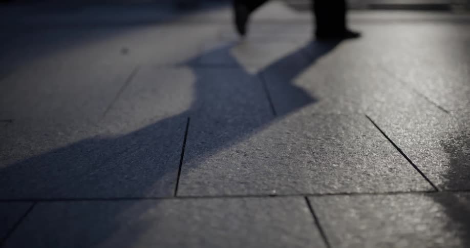 Pedestrians walking across a tiled walkway cast shadows on the ground