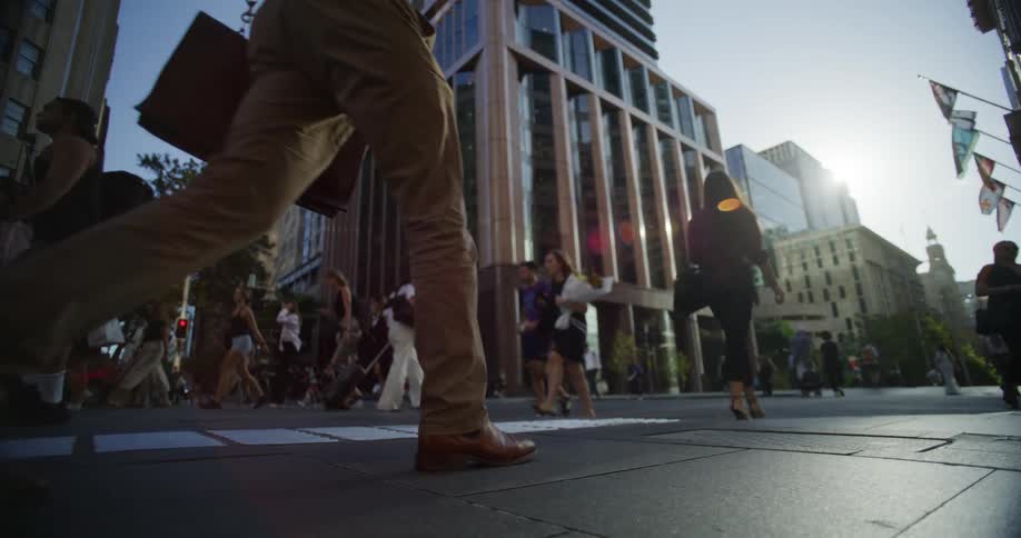 A crowd of pedestrians are walking on a wide sidewalk in a downtown metropolis on a sunny summer day