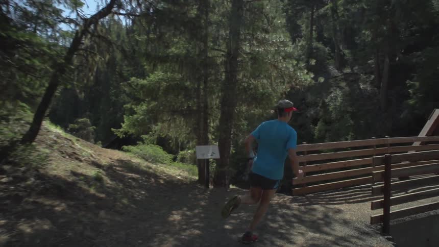A man running down a path and over a bridge in a mountain forest