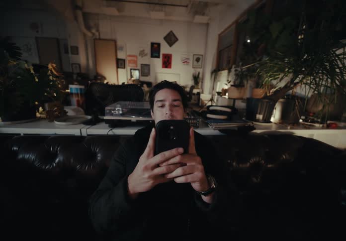 The face of a young man who is using a cell phone and he is sitting on a black sofa