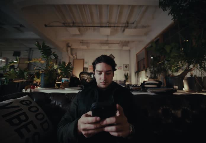 The face of a young man who is using a cell phone and he is sitting on a black sofa and then puts the cell phone aside