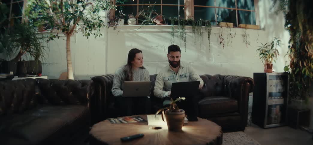 Two people talk while sitting in the living room with their laptops at night