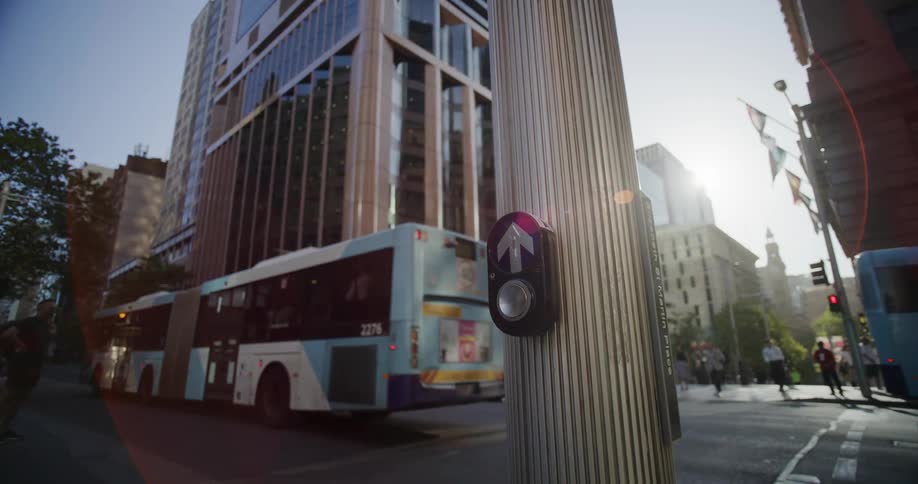 Pedestrians wait while an extended bus crosses through a downtown intersection on a sunny day