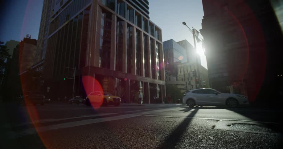 Urban intersection with modern buildings in the background moving cars and the low sun creating reflections and long shadows on the street