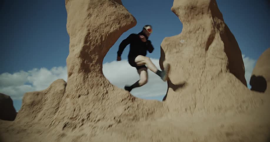 Man in sunglasses jumping and running between rock crevices