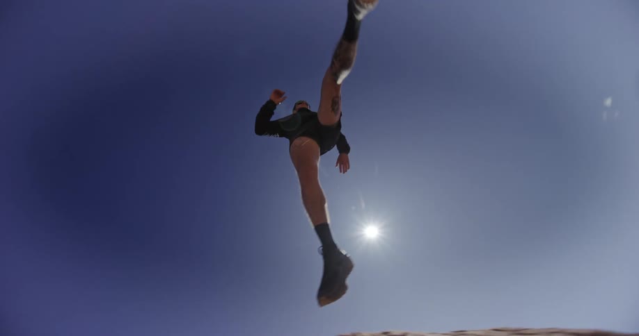 A person is running in a desert landscape jumping from one rock to another under a blue sky