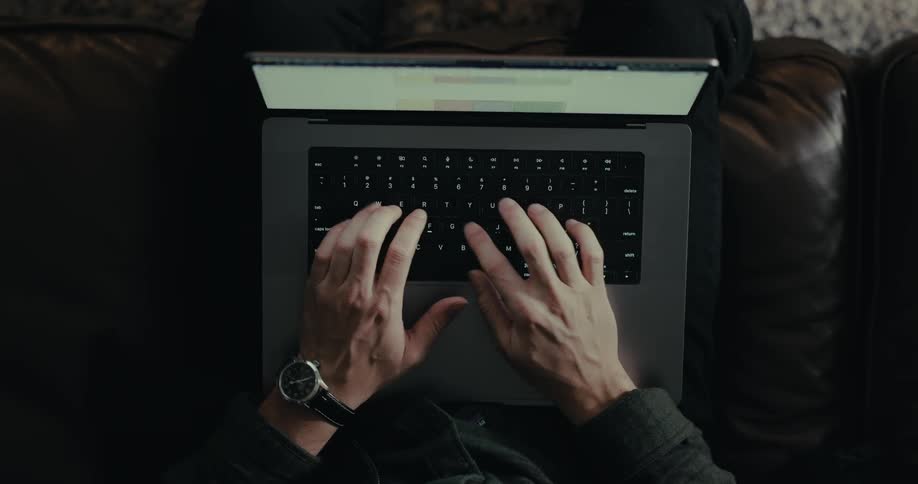 A person sitting on a couch opens a laptop and starts typing in the keyboard