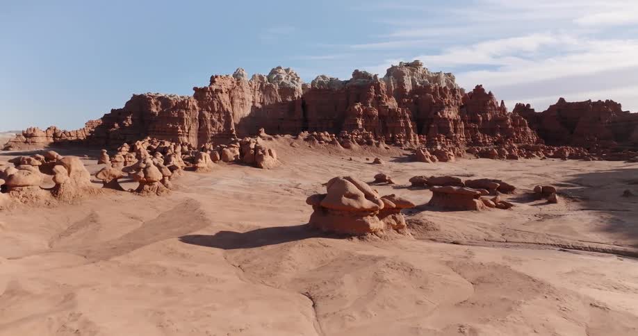 An aerial view flying backwards reveals a desert landscape of unique hoodoo rock formations in goblin valley