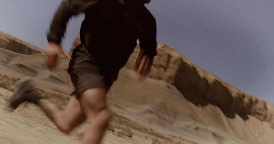 A person is running in a desert landscape with rugged hills in the background under a partly cloudy sky
