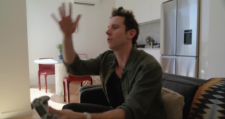 A man is sitting on a couch in a modern living room playing a video game