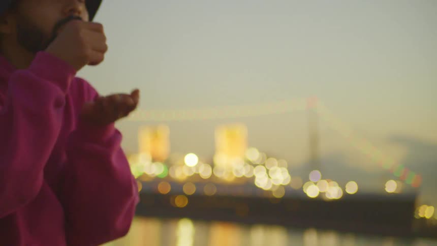 Man gestures and mimes an action while standing outdoors on the waterfront at night