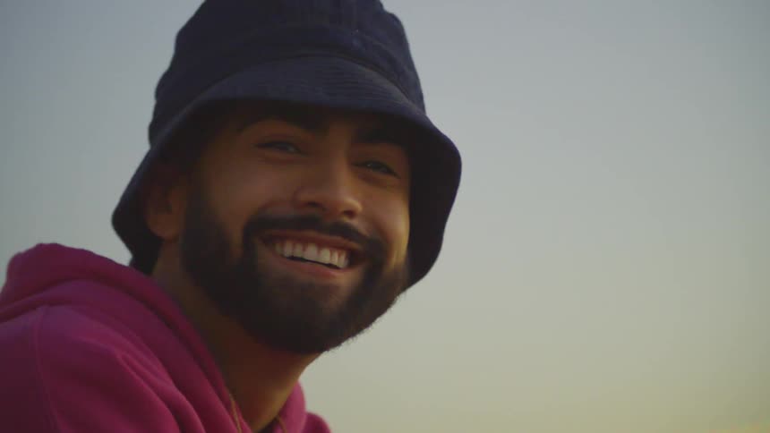 Cheerful man sitting in a square by a lake at dusk