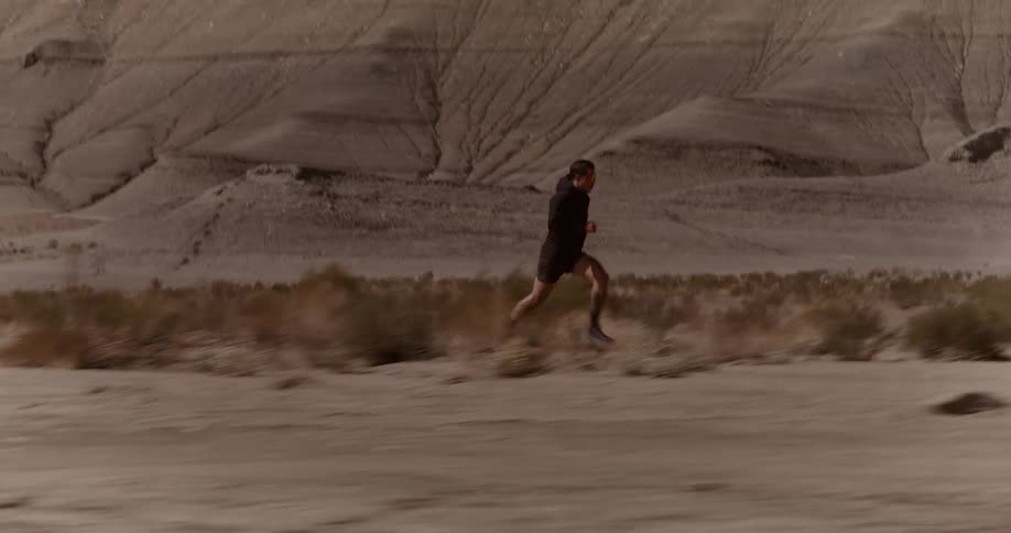 Man running very fast in a desert area with mountains in the background