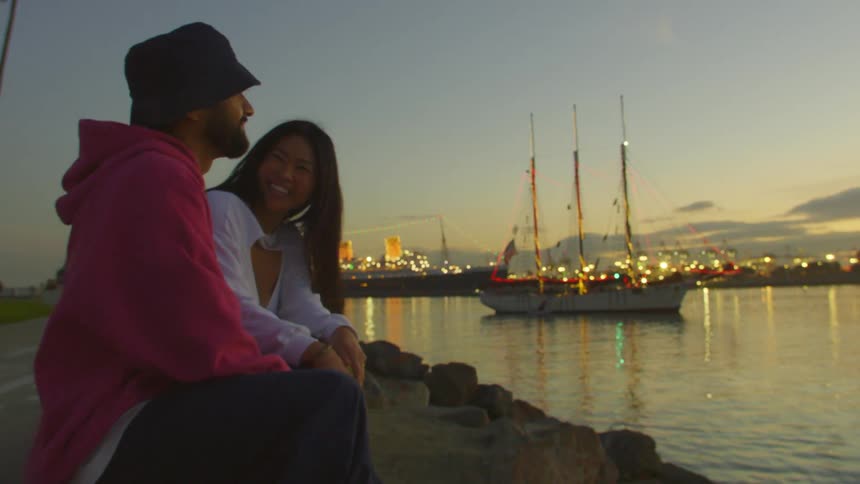A boat sails past a couple hugging on the shore