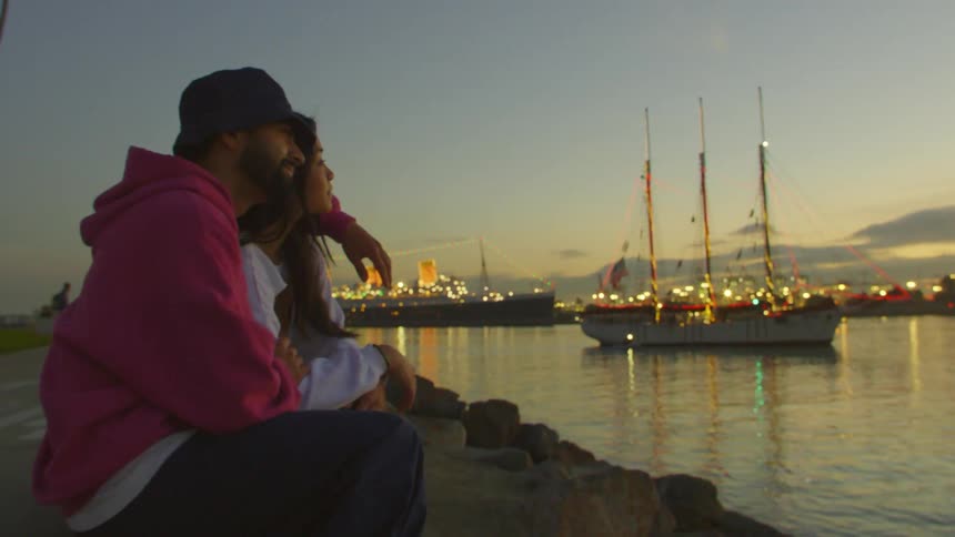 Cheerful couple sitting in a park by a lake with a boat in the background