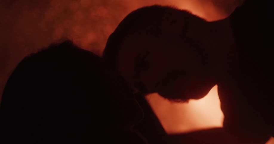 The silhouette of a couple kissing in front of a large bonfire at night