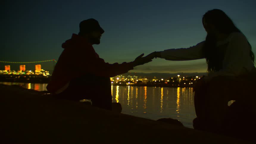 Silhouette of a couple holding hands by a lake at night
