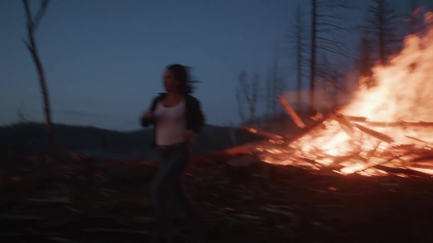 Woman running from a forest on fire at night