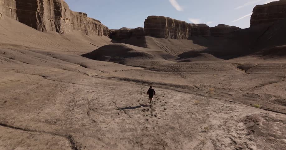 Person running in a desert landscape with rock formations in the background under a clear sky