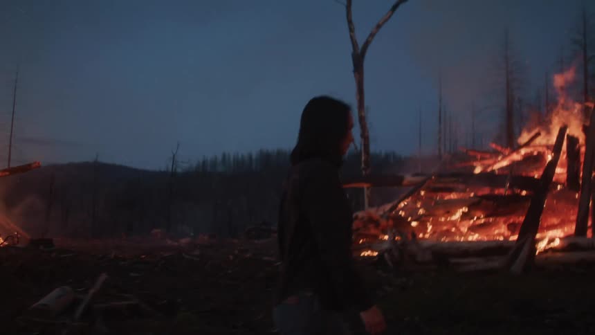Woman walking towards a large bonfire at night in the forest