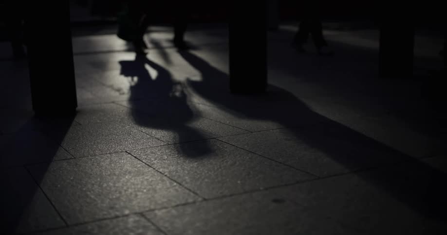 Elongated shadows of pedestrians projected onto the ground illuminated by the low sun their legs and feet moving
