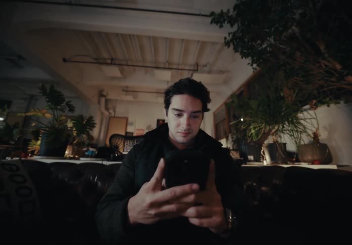 Man sitting in a room decorated with plants at night uses his smartphone