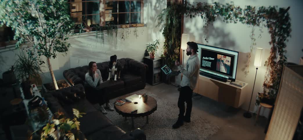 Man standing talking to a woman sitting on a couch next to a dog